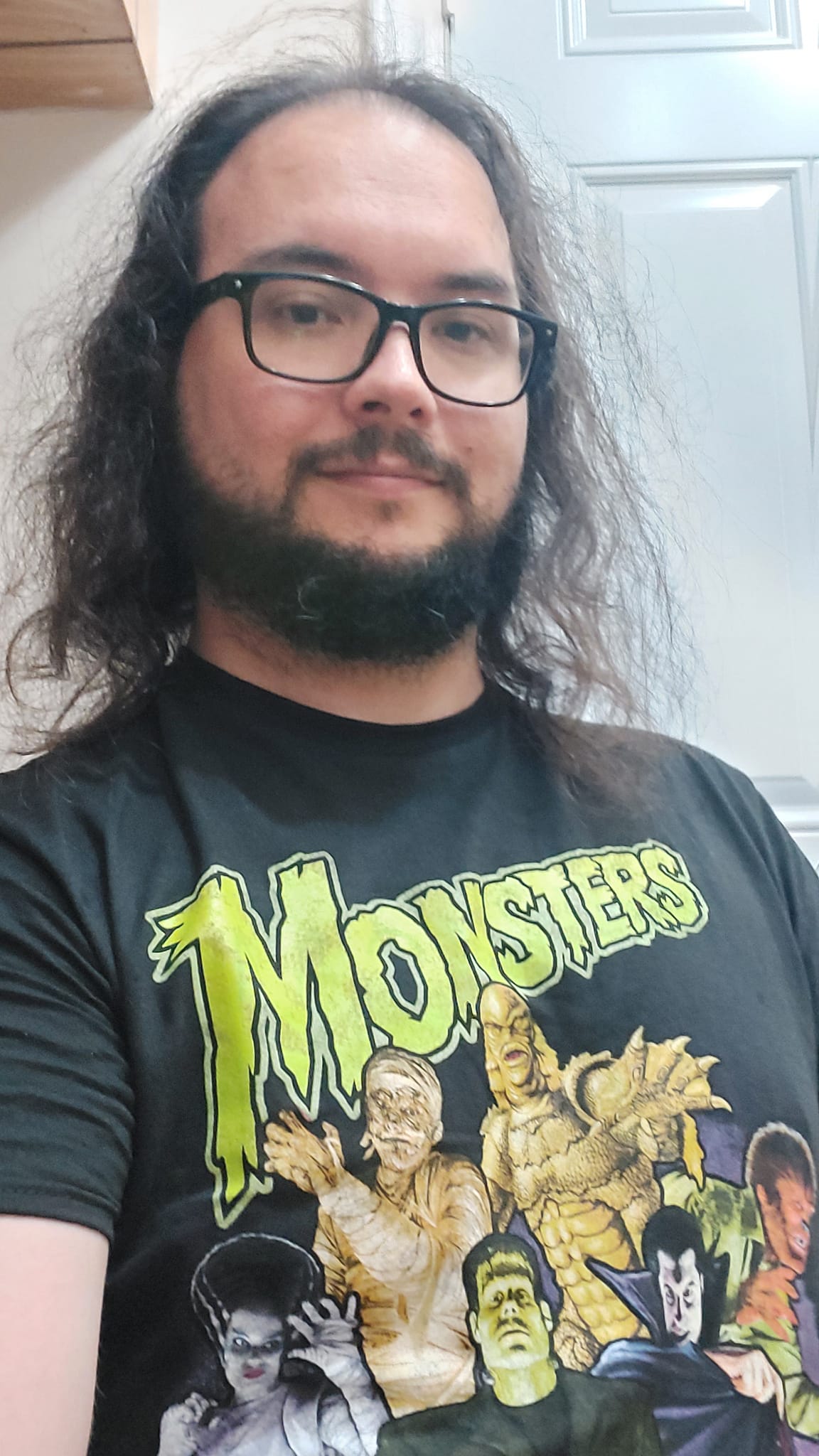 A man with long dark hair and a beard shows off his new t-shirt, featuring the classic Universal Monsters